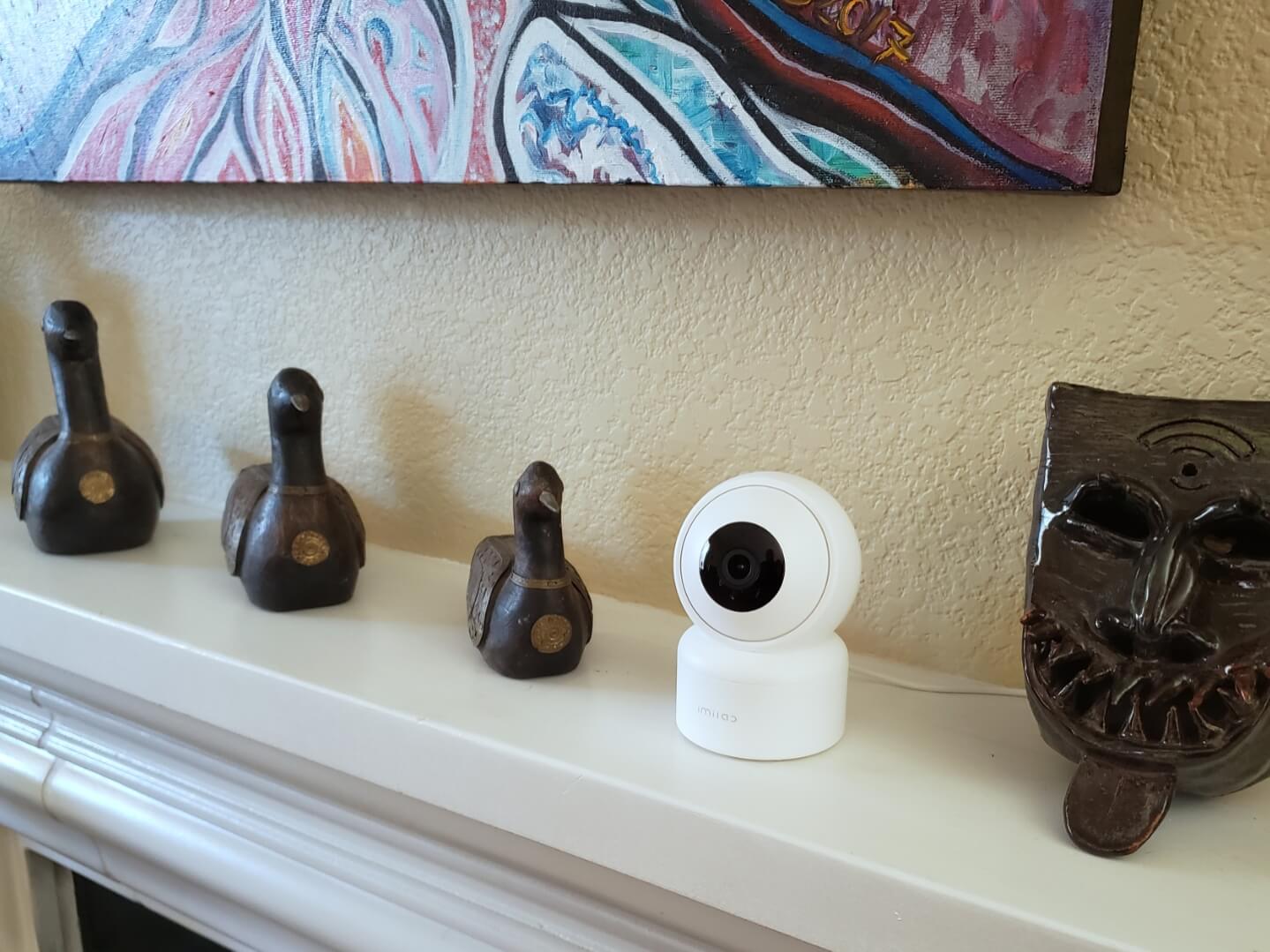 A home security camera and wood decorations shaped like birds, sitting on top of a fireplace mantle.